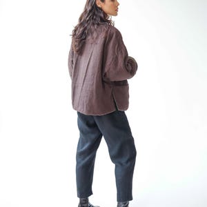 May include: A person wearing a brown linen jacket, black trousers, and black ankle boots. The jacket has a relaxed fit and a simple design. The trousers are a dark colour and have a slightly loose fit. The boots are leather.