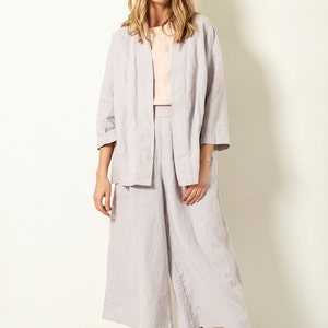 May include: A woman wearing a light purple linen outfit, consisting of a jacket, a top, and culottes. She is also wearing yellow sandals. The outfit is made of a soft, flowing fabric, perfect for warm weather.