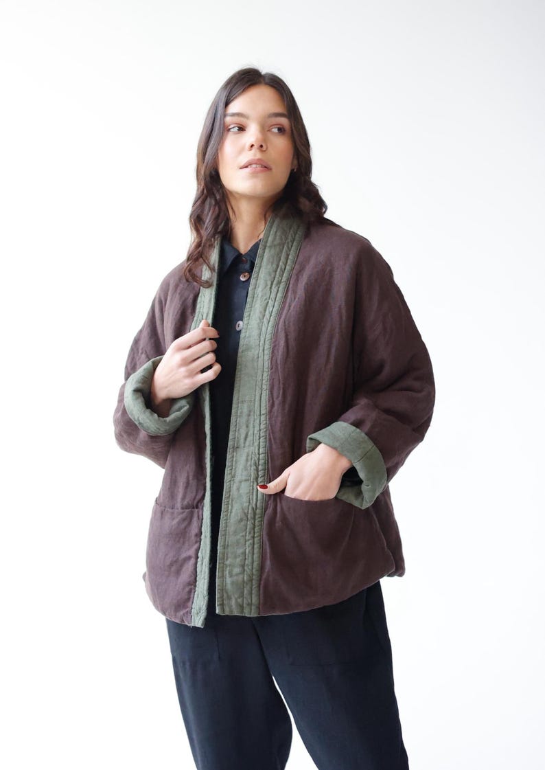 May include: A brown quilted jacket with olive green trim and cuffs. The jacket has a relaxed fit with pockets and is worn over a dark shirt and trousers. The jacket's color is a deep, earthy tone, and the trim provides a contrasting accent.