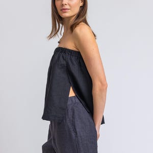 May include: A black strapless top with a split front and dark blue striped pants. The top is made of a soft, flowing fabric. The pants have a vertical stripe pattern.