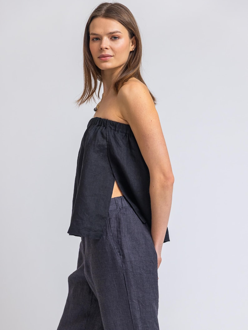 May include: A black strapless top with a split front and dark blue striped pants. The top is made of a soft, flowing fabric. The pants have a vertical stripe pattern.