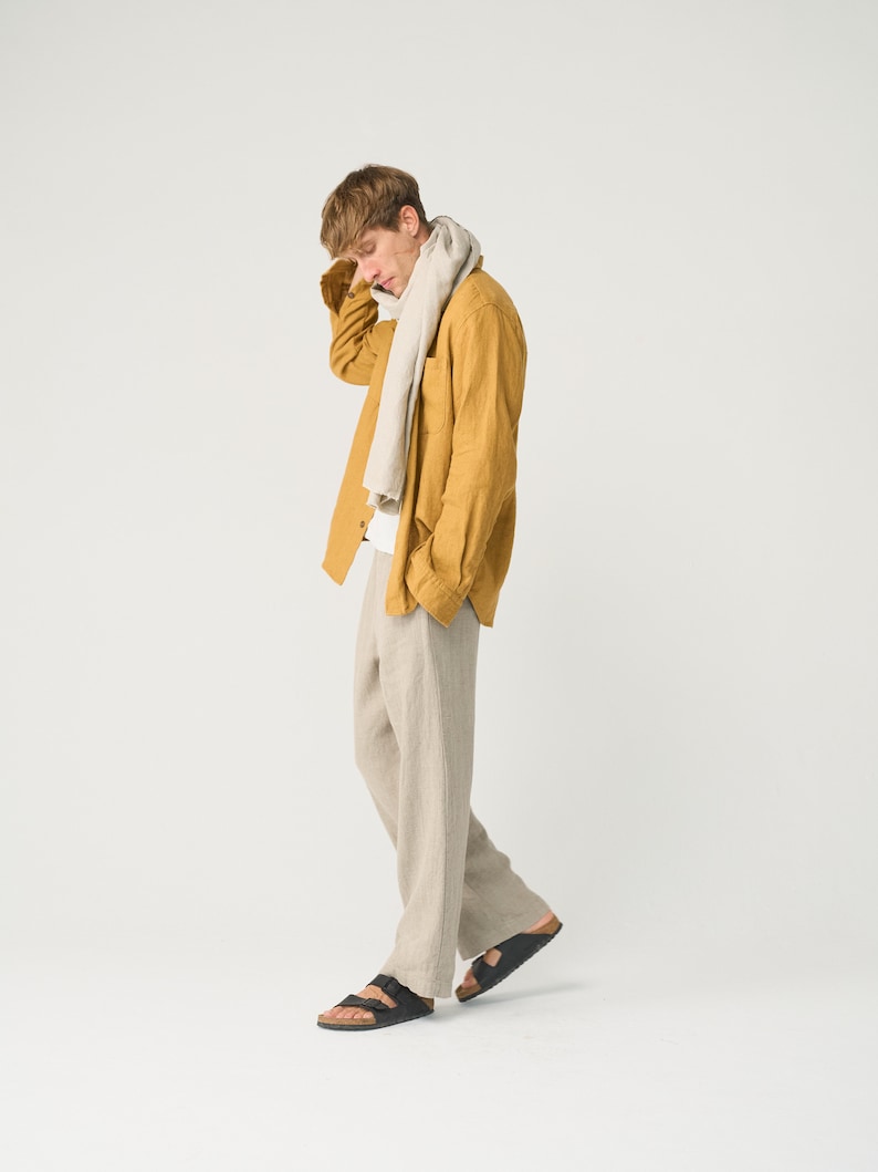 May include: A man wearing a mustard yellow linen shirt with a beige scarf, beige linen pants, and black sandals.