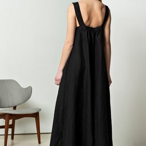 May include: A black linen maxi dress with thin straps and a gathered waist. The dress has a slightly A-line silhouette and a high neckline.