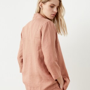 May include: A dusty rose linen blazer with three-quarter sleeves and matching pants. The blazer has a collared neckline and a relaxed fit. The outfit is made of a lightweight, textured fabric, perfect for a casual or semi-formal look.