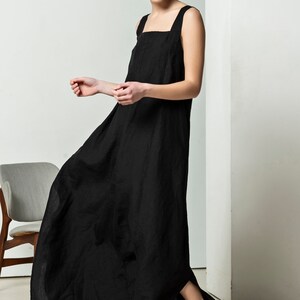 May include: A black linen maxi dress with a square neckline and thin straps. The dress has a side slit and a relaxed fit.
