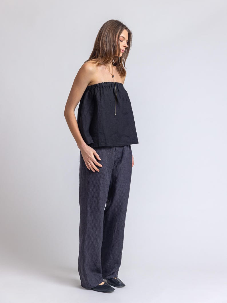 May include: A black strapless top and dark blue pants. The top has a gathered neckline and a drawstring. The pants are wide-legged and made of a similar fabric. The outfit is simple and elegant, suitable for various occasions.