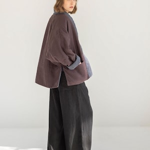 May include: A plum-coloured jacket with a blue collar and cuffs. The jacket has a relaxed fit and is worn with wide-leg black trousers. The outfit is simple and elegant, suitable for casual wear.