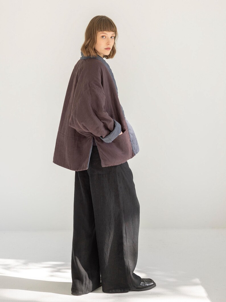 May include: A plum-coloured jacket with a blue collar and cuffs. The jacket has a relaxed fit and is worn with wide-leg black trousers. The outfit is simple and elegant, suitable for casual wear.