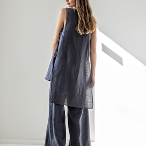 Puede incluir: Una t&uacute;nica de lino sin mangas y pantalones de lino de pierna ancha en color gris oscuro. La parte superior tiene un corte holgado y una longitud ligeramente m&aacute;s larga. Los pantalones tienen una pierna ancha y un corte recto.