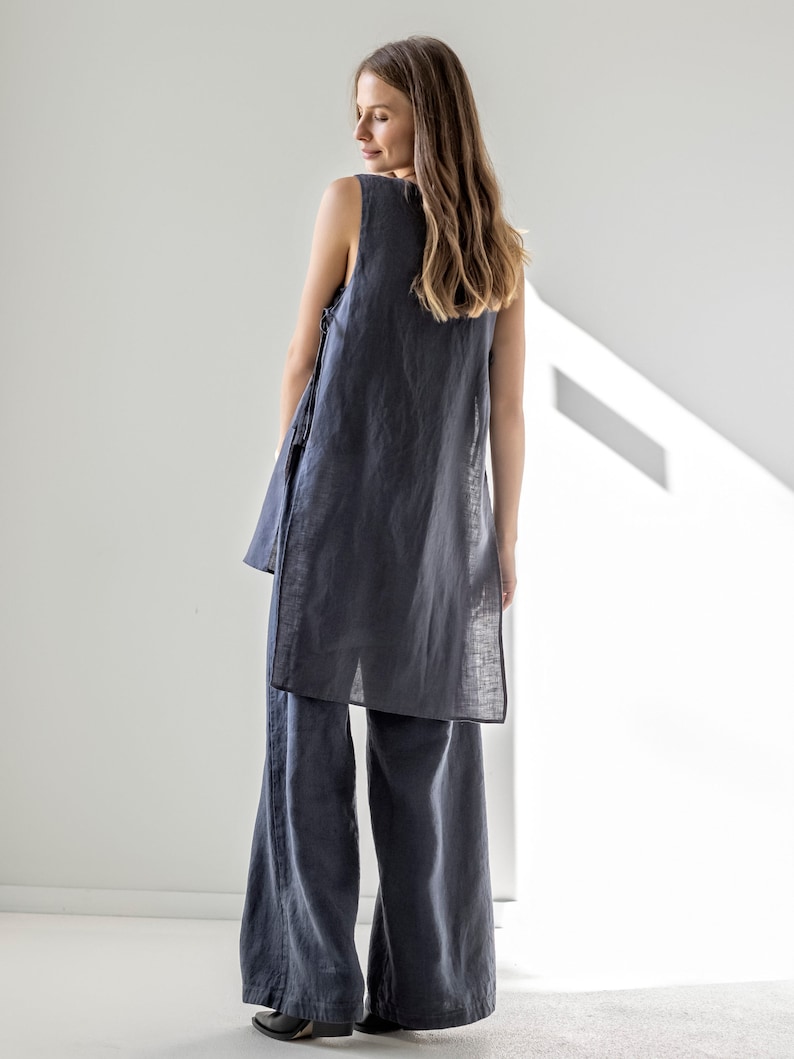 Puede incluir: Una t&uacute;nica de lino sin mangas y pantalones de lino de pierna ancha en color gris oscuro. La parte superior tiene un corte holgado y una longitud ligeramente m&aacute;s larga. Los pantalones tienen una pierna ancha y un corte recto.