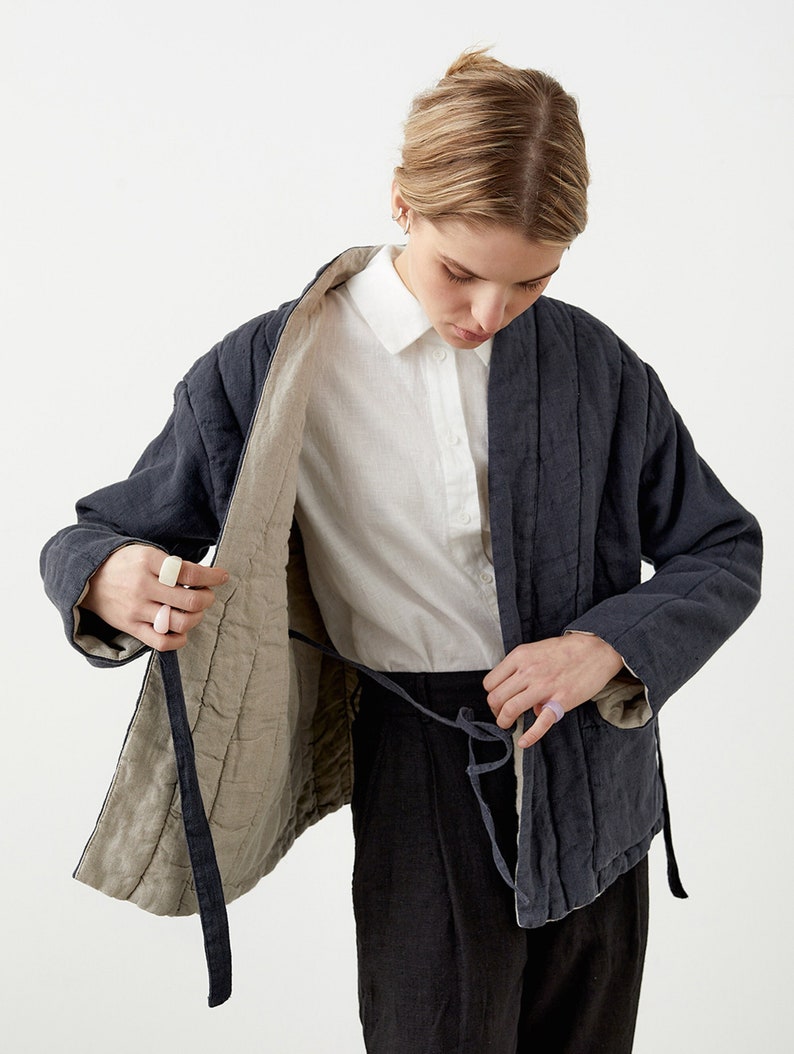 May include: A dark blue quilted jacket with a beige lining and a tie closure. The jacket is open, revealing a white button-up shirt underneath.