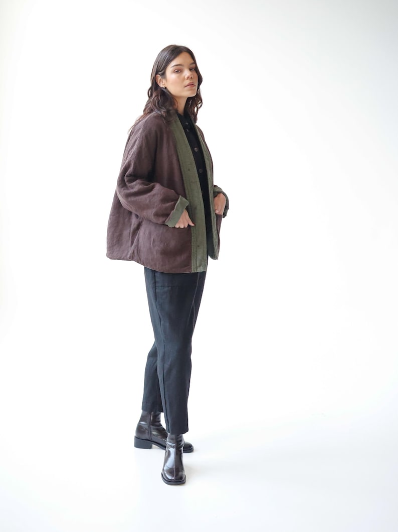May include: A brown jacket with green lining and trim. The jacket is worn over a black shirt and paired with black trousers and black boots. The jacket has a relaxed fit and a casual style.