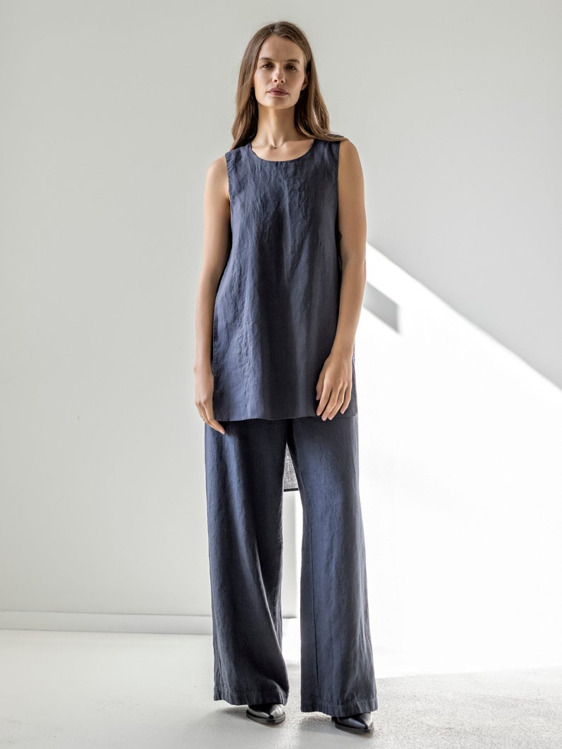 Puede incluir: Una blusa de lino sin mangas y pantalones de lino de pierna ancha en color gris oscuro. El conjunto es holgado y casual.