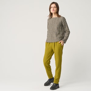 Può includere: Una persona indossa un top a maniche lunghe a quadri neri e beige e pantaloni verde oliva. La persona indossa anche mocassini neri. L'outfit è ambientato su uno sfondo bianco.