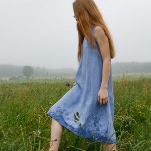 Puede incluir: Un vestido sin mangas de color azul b&iacute;garo, largo hasta la rodilla, con escote redondo y una silueta holgada y relajada. La tela parece ligera y presenta un tejido texturizado sutil, con manchas de humedad visibles en el dobladillo.