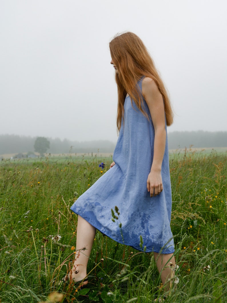 Puede incluir: Un vestido sin mangas de color azul b&iacute;garo, largo hasta la rodilla, con escote redondo y una silueta holgada y relajada. La tela parece ligera y presenta un tejido texturizado sutil, con manchas de humedad visibles en el dobladillo.