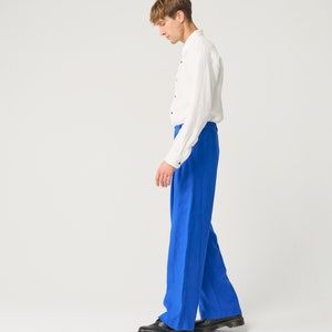 May include: A person wearing a white linen shirt and blue linen pants. The person is wearing black shoes.