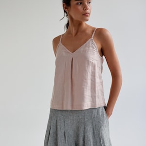May include: A light pink camisole top with thin straps and a V-neck, paired with gray linen culottes. The top has a pleated detail at the neckline. The pants are high-waisted and wide-legged.