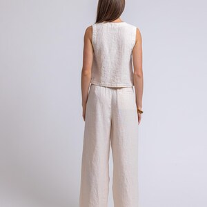 May include: A sleeveless, cream-colored linen top and wide-leg pants set. The outfit is made of a textured fabric and has a relaxed fit. The model is facing away from the camera, showcasing the back of the outfit.