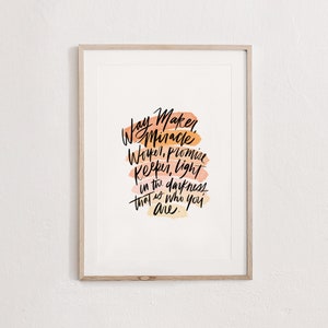 May include: A framed print with a watercolor background in shades of orange and pink. The print features a handwritten quote that reads "Way Maker, Miracle Worker, Promise Keeper, Light in the darkness that is who you are."