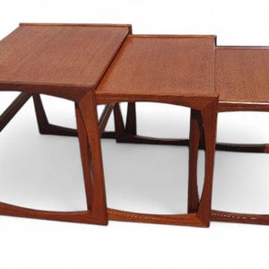 May include: A set of three nesting tables made of wood. The tables are rectangular and have a light brown finish. The tables are stacked on top of each other, with the largest table on the bottom and the smallest table on top.