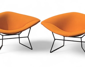 May include: Two orange lounge chairs with black wire frames. The chairs are designed with a deep, curved seat and a wide, square back.