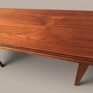 May include: A rectangular wooden coffee table with a rich reddish-brown grain pattern. The table features a flat, smooth top surface and four angled, tapered legs that extend outward from the center, providing a stable base for the furniture.