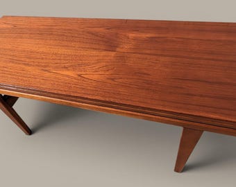Puede incluir: Una mesa de centro rectangular de madera con un rico patrón de vetas de color marrón rojizo. La mesa presenta una superficie superior plana y lisa y cuatro patas anguladas y cónicas que se extienden hacia afuera desde el centro.