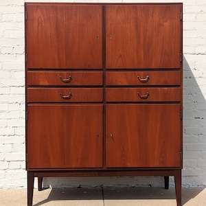 May include: A vintage wooden cabinet with two doors and four drawers. The cabinet is made of dark wood and has brass handles. The cabinet is standing on four legs.