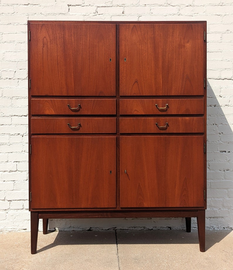 May include: A vintage wooden cabinet with two doors and four drawers. The cabinet is made of dark wood and has brass handles. The cabinet is standing on four legs.