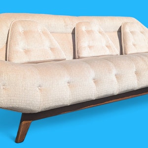 May include: A white tufted sofa with three back cushions and a wood frame. The sofa has a unique, curved shape and is on a blue background.