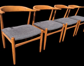 May include: Four wooden chairs with grey fabric seats. The chairs have a curved back and a simple design.