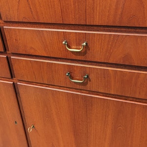 May include: A wooden cabinet with four drawers and two doors. The drawers have brass handles and the doors have a keyhole. The cabinet is made of a dark wood with a natural grain.