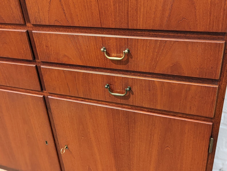 May include: A wooden cabinet with four drawers and two doors. The drawers have brass handles and the doors have a keyhole. The cabinet is made of a dark wood with a natural grain.