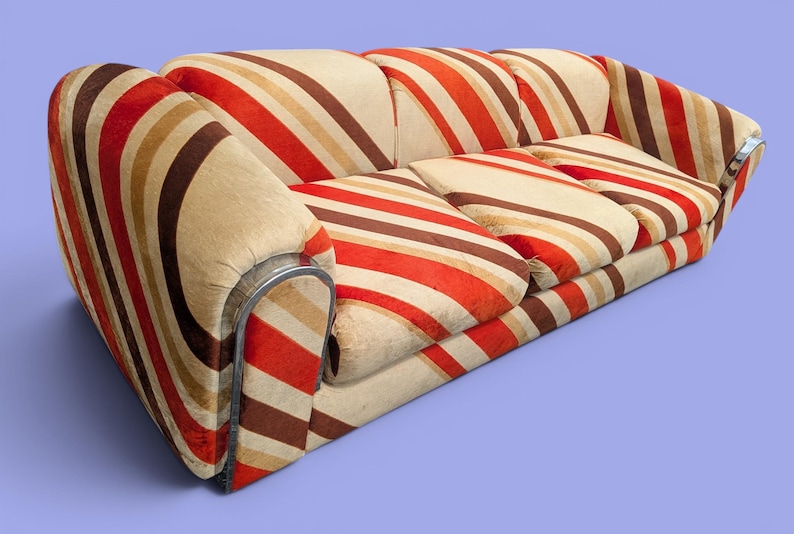 May include: A retro-style sofa with a striped pattern in shades of brown, beige, and red. The sofa has rounded arms with a silver metal trim. The cushions also feature the same striped design. A unique piece of furniture.