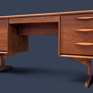 May include: A wooden desk featuring a rectangular top and two side pedestals, each containing three drawers with elongated, tapered wooden handles. The desk is supported by two angled, T-shaped wooden legs that extend outward from the base.