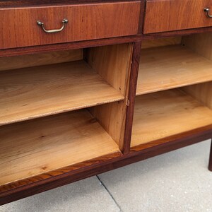 May include: A wooden cabinet with two drawers and two doors. The doors are open, revealing two shelves inside. The cabinet is made of dark wood with a light wood interior.