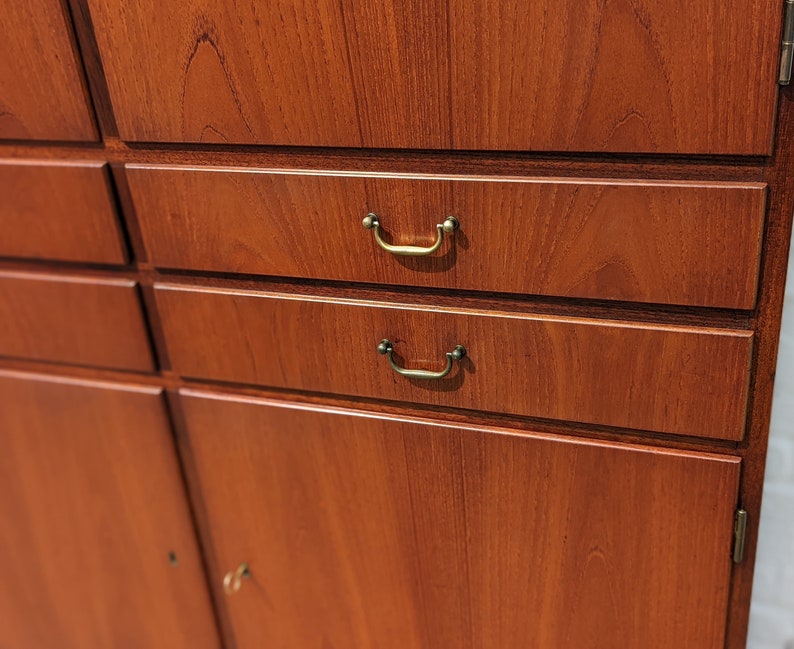 May include: A wooden cabinet with multiple drawers and doors. The cabinet has a light brown wood finish and brass hardware. The drawers have simple, rectangular pulls.