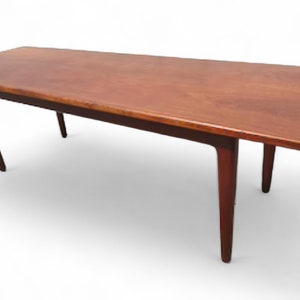 May include: A long, rectangular, wooden coffee table with a dark brown finish. The table has four legs that taper towards the bottom.
