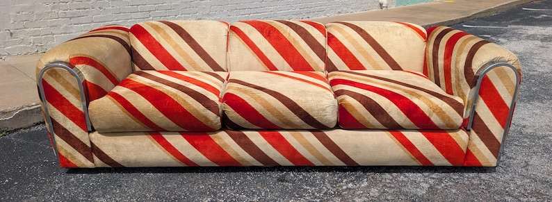 May include: A three-cushion sofa with a distinctive striped pattern in red, brown, and beige. The sofa has rounded arms and a low profile, offering a vintage aesthetic. The stripes run diagonally across the cushions and frame.