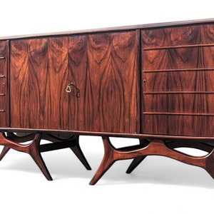 May include: A mid-century modern sideboard with a rich mahogany finish. It features three doors, two with drawers and one with a single door. The sideboard has unique, curved legs.
