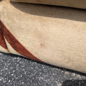 May include: Close-up of a section of a beige upholstered sofa with a brown and orange striped pattern. The fabric appears to be soft and textured. The sofa is likely vintage or retro in style.