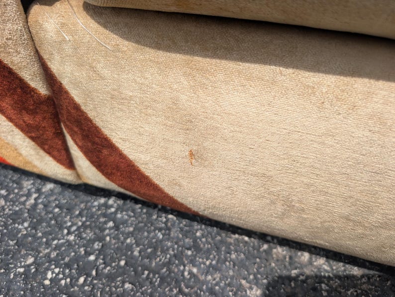 May include: Close-up of a section of a beige upholstered sofa with a brown and orange striped pattern. The fabric appears to be soft and textured. The sofa is likely vintage or retro in style.