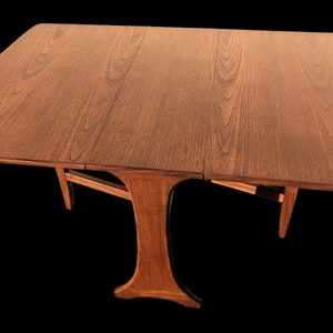 May include: A brown wooden extendable dining table with a unique, sculptural base. The table top is made of wood with a natural grain pattern.