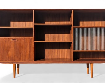 May include: A mid-century modern teak wood bookcase with a glass door and a closed cabinet door. The bookcase has multiple shelves and is supported by four tapered legs.