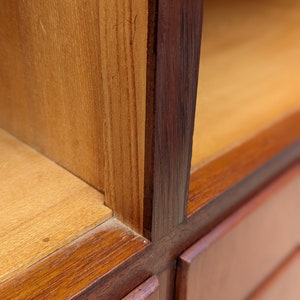 May include: Close-up of a wooden cabinet with a dark brown finish. The cabinet has multiple shelves and drawers. The wood grain is visible on the surface.