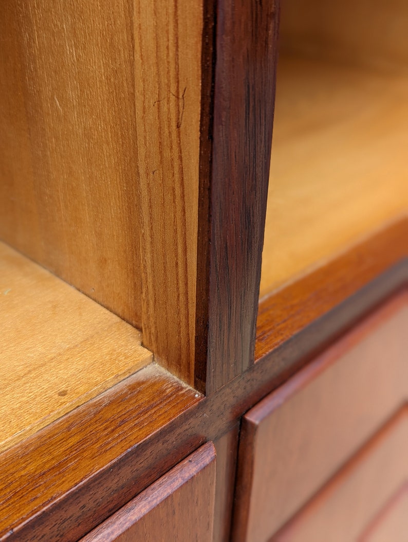 May include: Close-up of a wooden cabinet with a dark brown finish. The cabinet has multiple shelves and drawers. The wood grain is visible on the surface.