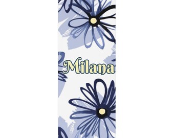 May include: A white bookmark with a blue floral pattern and the name "Milana" in yellow lettering.