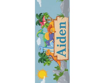 May include: A blue and green dinosaur themed door sign with the name Aiden on a wooden sign. The sign is surrounded by dinosaurs and palm trees.