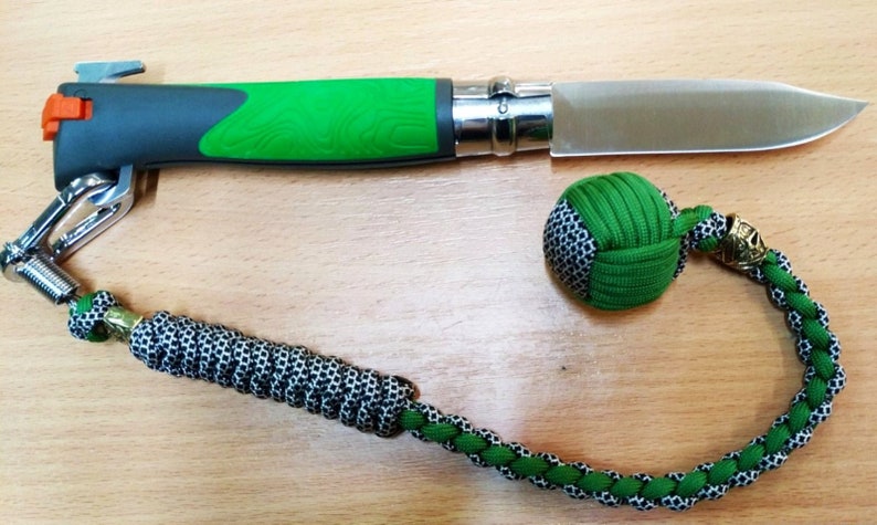 May include: A green and black paracord keychain with a green and black ball at the end. The keychain is attached to a green and gray folding knife with a silver blade.
